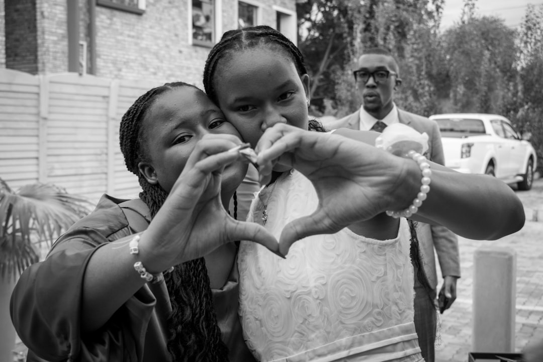 Two girls make heart shape with hands, man watches.