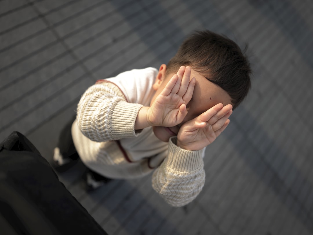 A young child covers their face with hands.