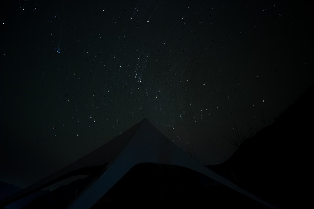 Stars shine brightly over dark desert dunes at night.