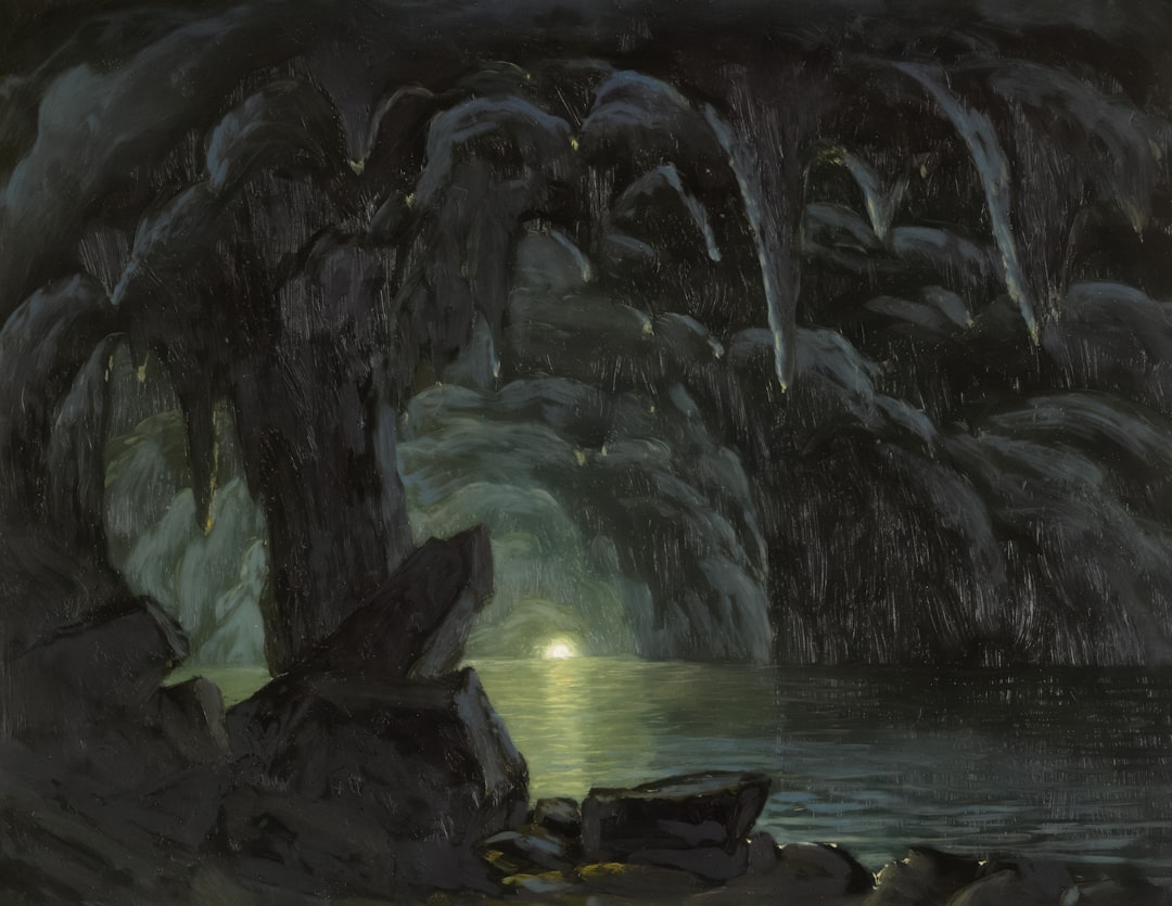 Dark cave opening with sunlight reflecting on water.